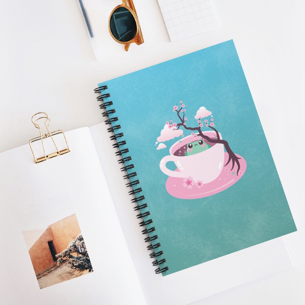 spiral notebook journal planner with a kawaii cute green frog sitting in a pink tea cup with pastel japanese sakura cherry blossom tree and petals with clouds in the sky