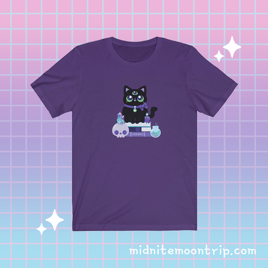 t shirt with a 3-eyed black cat witch with a spooky crystal skull, a magic potion, and a melting candle sitting on a stack of spellbooks